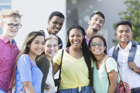 a group of high school students standing together and smiling outside on the school lawn